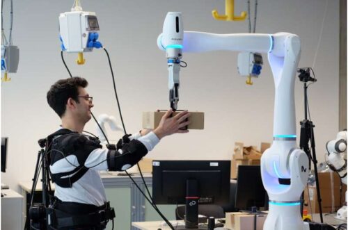 Researcher Federico Masiero receives a package whose weight the robot has already transmitted to the exoskeleton. Credit: Andreas Schmitz / TUM