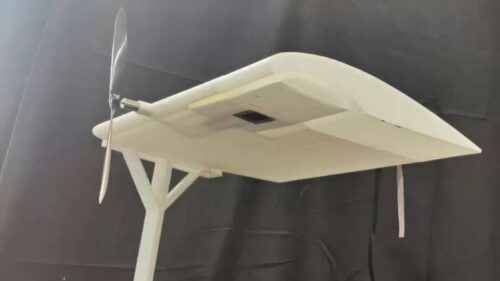 A prototype laser-powered receiver integrated beneath the wing of a stationary drone model converts energy from a green laser into electricity while airflow generated by the propeller carries heat away through built-in cooling channels.