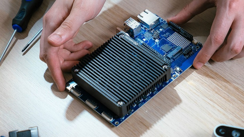 Close-up of an Arduino board with heatsink being fitted by hand during assembly