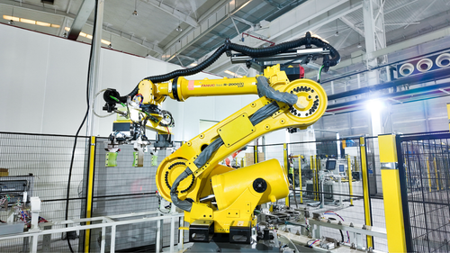 Yellow industrial robotic arm handling parts inside a fenced automated production line at EnerVenue's battery factory