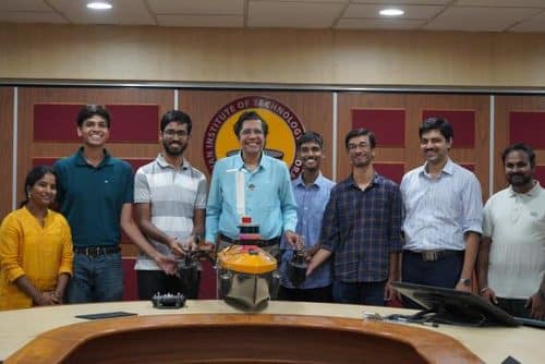 Members of IIT Madras's Team Aritra and faculty standing with the autonomous boat on a table in a meeting room at the institute