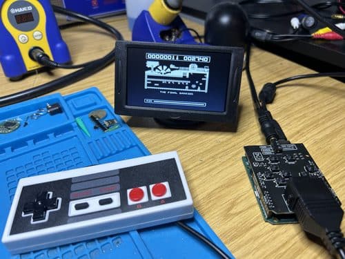 Custom retro gaming controller and circuit board connected to a small display running Manic Miner on an electronics workbench.