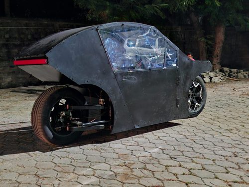 Side view of the Jedlik Motors E-Pod prototype, a futuristic black enclosed electric two-wheeler parked outdoors.