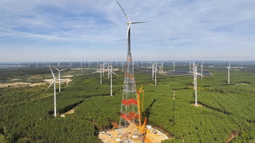 The lattice tower of the 365-metre wind turbine during construction, with a large crane beside it and conventional turbines in the background