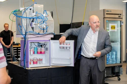 Engineer demonstrating a prototype refrigerator containing beverage cans